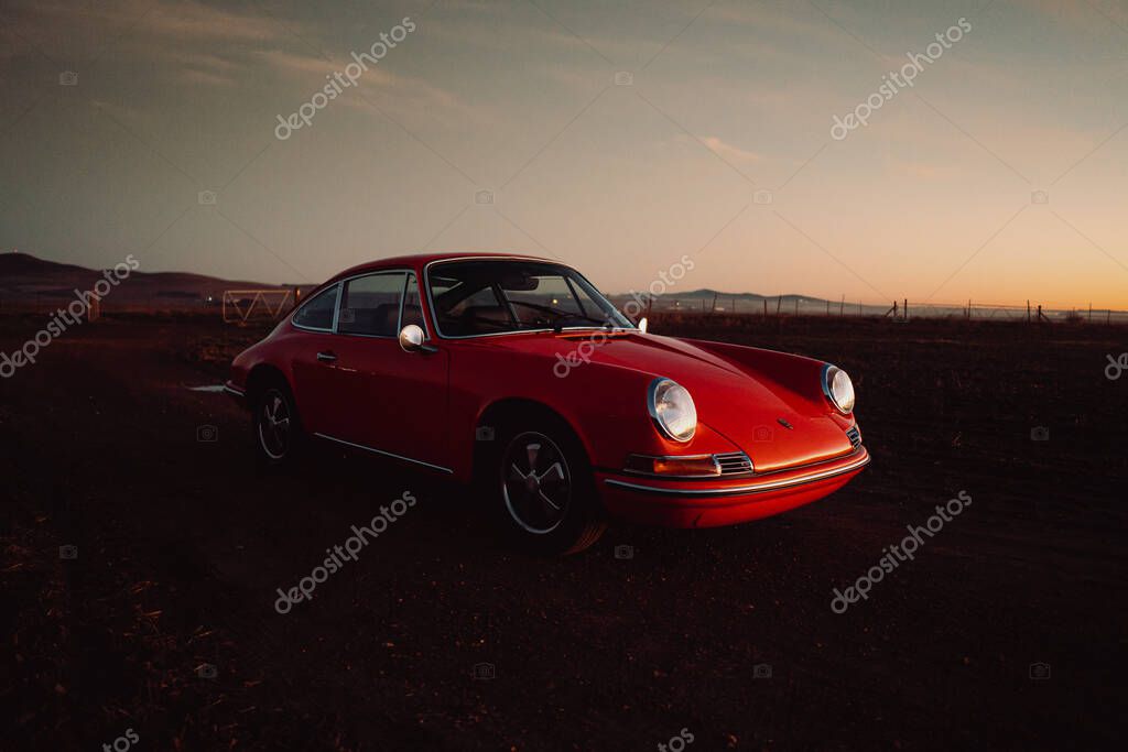 A closeup shot of a classic red Porsche 912 vintage car in the field at sunset