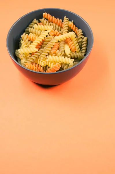 在橙色背景上隔离的碗上垂直拍摄的三色罗蒂尼面食 — 图库照片