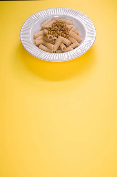 黄色の背景に隔離されたプレート上に緑のエンドウ豆とリガトーニパスタの垂直ショット — ストック写真