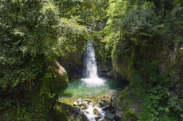 日光の下で森の中の岩や緑に囲まれた滝 — ストック写真