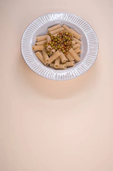 茶色の背景に隔離されたプレート上に緑のエンドウ豆とリガトーニパスタの垂直ショット — ストック写真