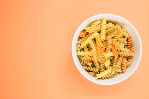 将未煮熟的三色罗提尼意大利面放在一个孤立于橙色背景的碗上的顶部视图 — 图库照片
