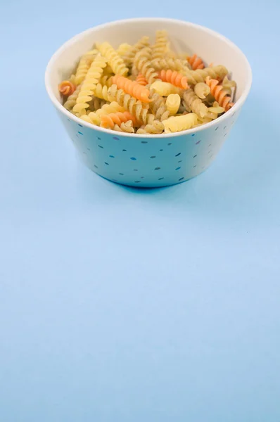 在蓝色背景隔离的碗上垂直拍摄的未煮熟的三色红辣椒面食 — 图库照片