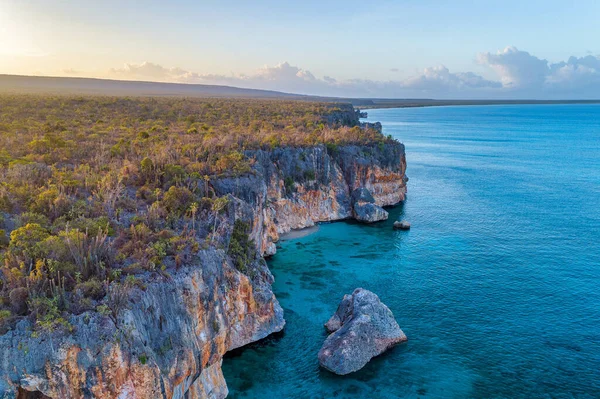日の出の海に囲まれた緑に覆われた岩場の崖の風景 — ストック写真