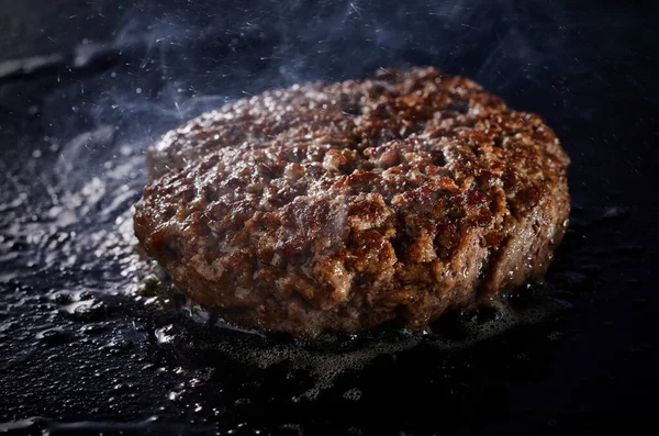 A thick juicy minced beef patty for a traditional burger grilling on a griddle