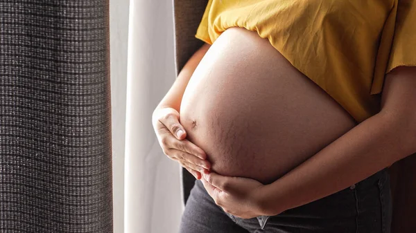 妊娠中の女性が室内に立って腹を抱えて — ストック写真