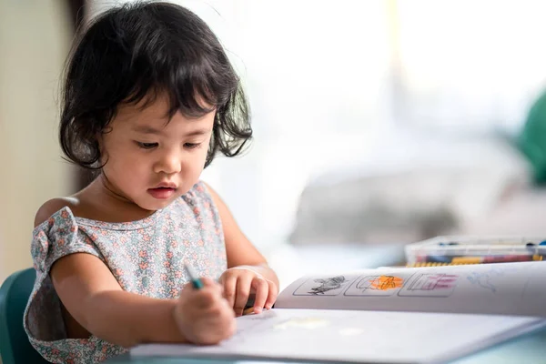 一个可爱的小女孩聚精会神地画在桌上的书上 — 图库照片