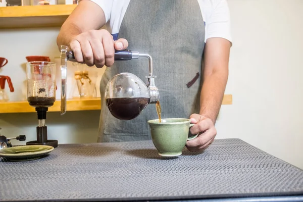 A man pouring coffee in the cup from a siphon coffee maker