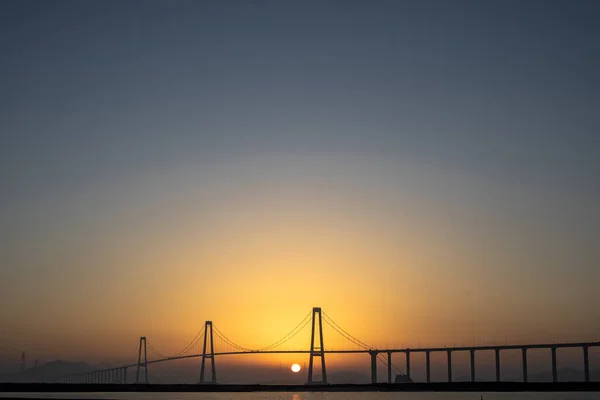 韓国の海に架かる大きな橋の後ろに沈む明るい太陽の高い角度のショット — ストック写真