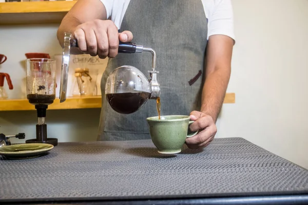 A man pouring coffee in the cup from a siphon coffee maker