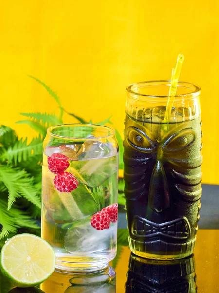 A vertical shot of cold cocktails in fancy glasses with a half of lime on a glass table