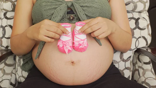 Closeup Shot Pregnant Female Lying Couch Holding Pink Baby Shoes — Stock Photo, Image