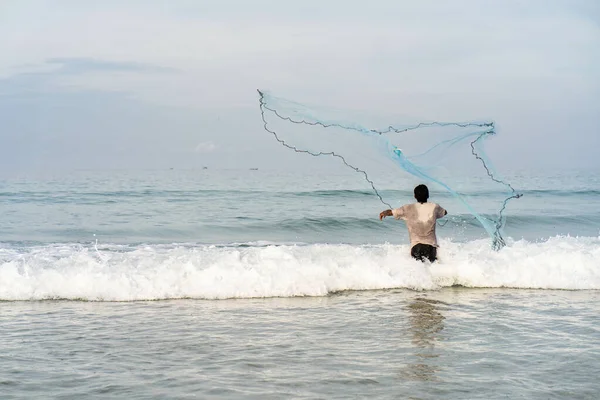 渔夫站在岸上 把渔网扔进海里捕鱼 — 图库照片