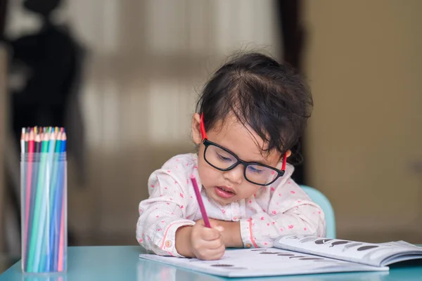 一个戴着眼镜的可爱的泰国小女孩在桌子上画着她的书 — 图库照片