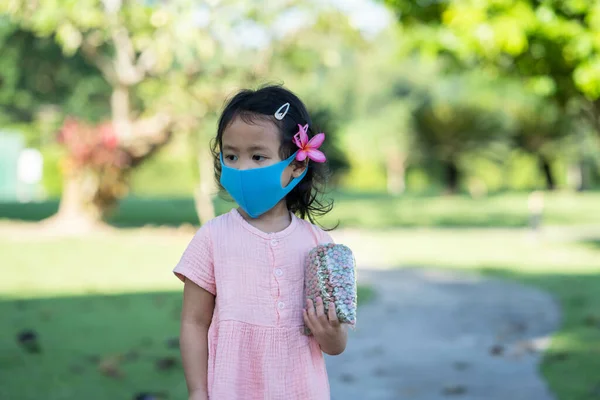 医療用マスクをした可愛い女の子が屋外でカラフルなシリアル付きの小さなビニール袋を持って歩く — ストック写真