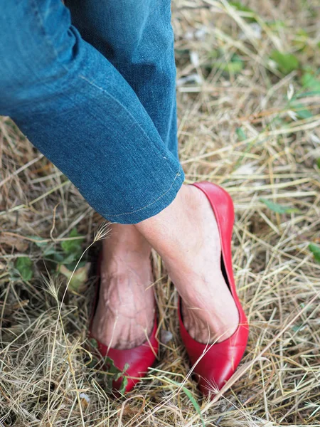 草の上に立つジーンズと赤いスカーピンのフラットを身に着けている女性の垂直ショット — ストック写真