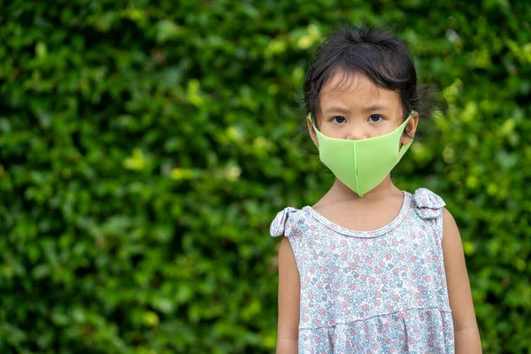 植物の壁の前に立っている彼女の顔にマスクを持つ美しい東南アジアの女性の子供 — ストック写真