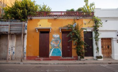 CARTAGENA, COLOMBIA - Jul 26, 2021: A painting of a woman in traditional clothing on yellow house in art district of Cartagena Colombia clipart