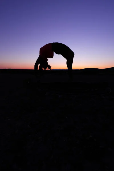 10代の少女のシルエットの垂直ショットを行使し ジャンプし 日没で体操を行う — ストック写真