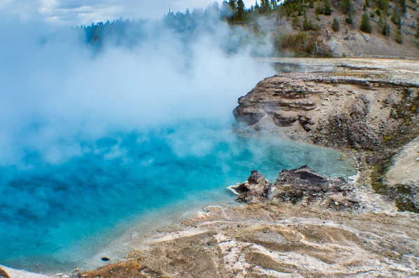 从靠近森林的岩石旁边的盆地间歇泉中喷出的蒸汽 — 图库照片