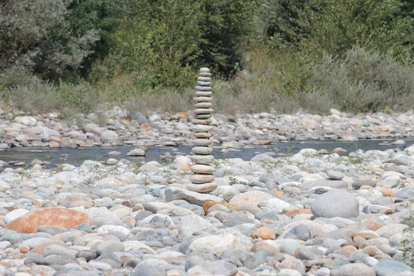 a stone cairn made out of round rocks by river in the dense forest