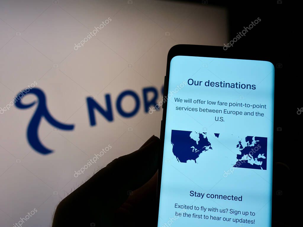 STUTTGART, GERMANY - Aug 15, 2021: Person holding cellphone with webpage of airline Norse Atlantic Airways on screen in front of logo. Focus on center of phone display.