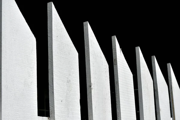 A painted, white picket fence against a black background.