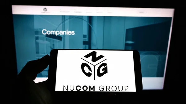 Stuttgart ドイツ 2021年8月14日 ドイツの持株会社Ncg Nucom Group Seのロゴが入った携帯電話をビジネスWebページの前で画面に表示する人 電話ディスプレイに焦点を当てる — ストック写真