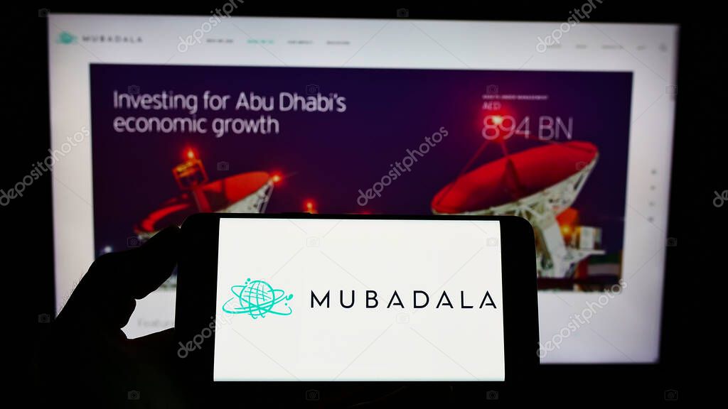 STUTTGART, GERMANY - Aug 23, 2021: Person holding mobile phone with logo of Emirati investor Mubadala Investment Company PJSC on screen in front of web page. Focus on phone display.