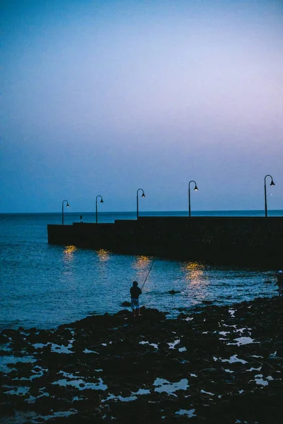 Homem Com Uma Vara Pesca Sobre Rochas Perto Mar Noite — Fotografia de Stock