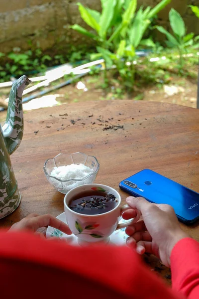 庭の木のテーブルの上にコーヒードリンク スマートフォンの手の近くに — ストック写真