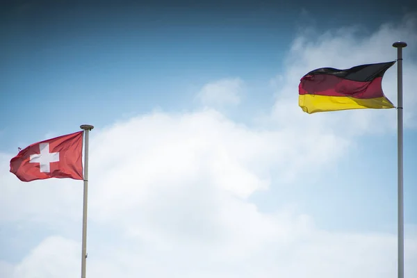 Švýcarské Německé Vlající Vlajky Kovové Tyči Proti Zatažené Modré Obloze — Stock fotografie