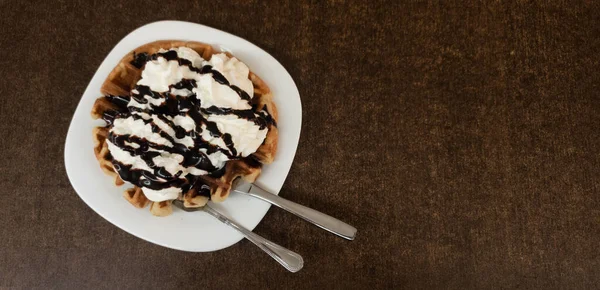 木のテーブルの上にクリームとチョコレートで覆われたワッフルを食欲をそそる — ストック写真