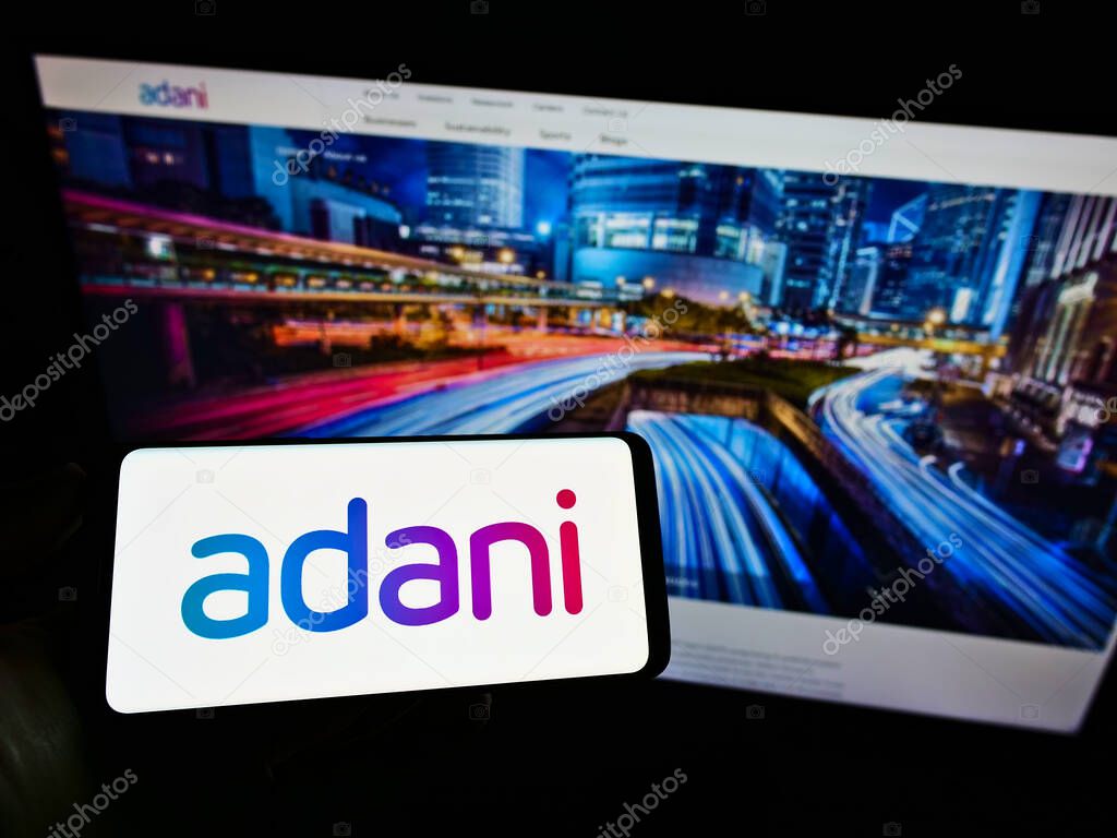 STUTTGART, GERMANY - May 31, 2021: Person holding mobile phone with logo of Indian conglomerate Adani Group on screen in front of business web page. Focus on phone display.