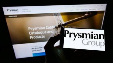STUTTGART, GERMANY - May 30, 2021: Person holding mobile phone with logo of Italian electric cable manufacturer Prysmian SpA on screen in front of web page. Focus on phone display. clipart