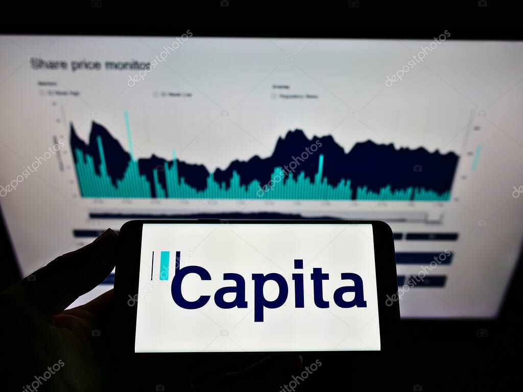 STUTTGART, GERMANY - May 23, 2021: Person holding smartphone with business logo of British process outsourcing company Capita plc on screen in front of website. Focus on phone display.