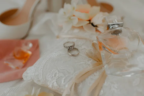 有一对结婚戒指和香水的垫子 周围都是婚纱 放在桌上 — 图库照片