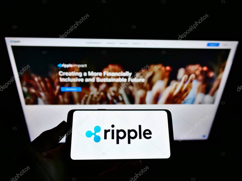 STUTTGART, GERMANY - May 22, 2021: Person holding smartphone with logo of American technology company Ripple Labs Inc. on screen in front of website. Focus on phone display.
