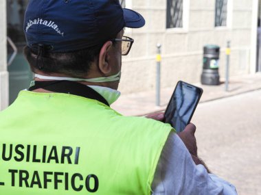 LOMBARDY, ITALY - Aug 19, 2021: A parking warden attendant from a private outsourced company issuing parking violations online printing and leaving the fine on the windscreen clipart