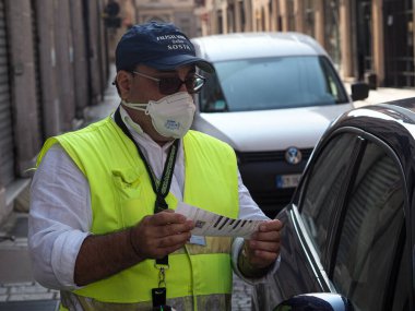 LOMBARDY, ITALY - Aug 19, 2021: A parking warden attendant from a private outsourced company issuing parking violations online printing and leaving the fine on the windscreen clipart