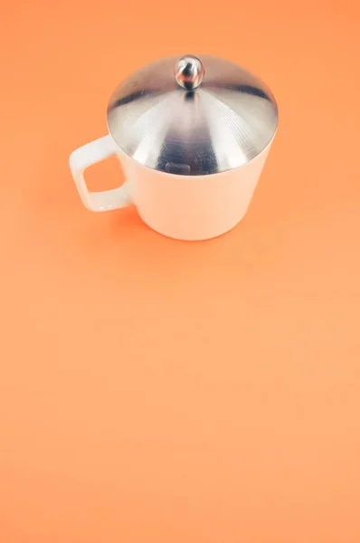 オレンジの背景に蓋のあるマグカップの垂直ショット — ストック写真