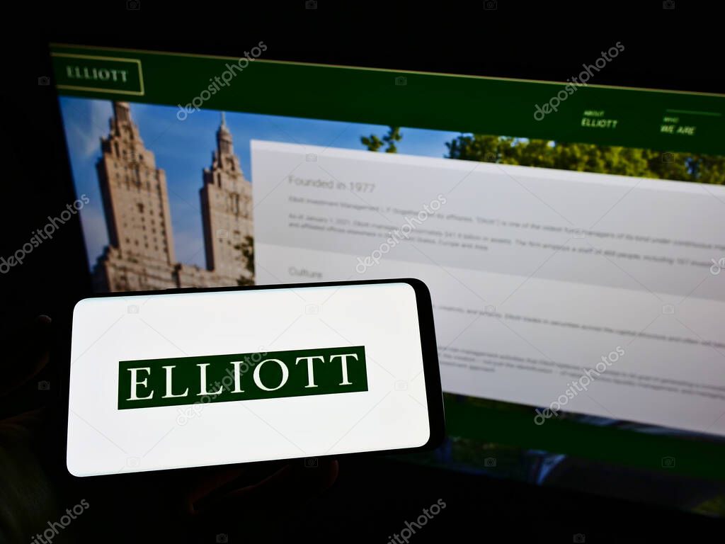 STUTTG, GERMANY - Jun 08, 2021: Person holding mobile phone with logo of US investment firm Elliott Management Corporation on screen in front of web page. Focus on phone display.