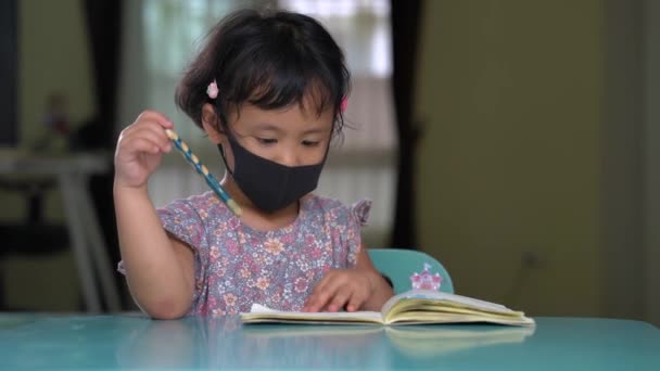 Маленькая Азиатка Маске Сидит Столом Переворачивает Страницы — стоковое видео