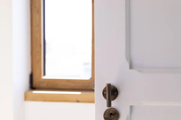 A closeup of a white painted wooden door with a metal door handle in the bedroom