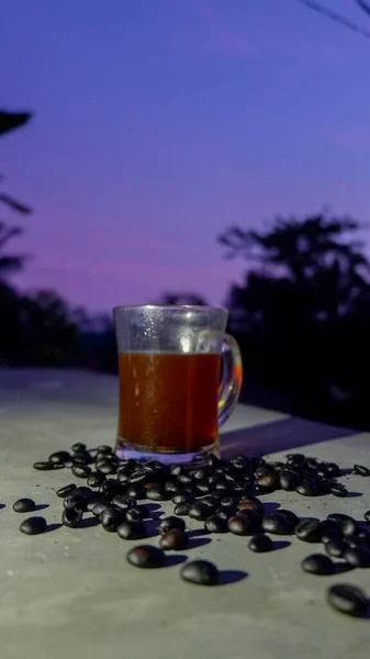 一杯黑咖啡的垂直镜头 在紫色的夕阳西下 咖啡周围散落着烤咖啡豆 — 图库照片