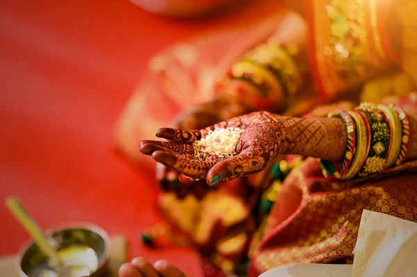 a female hand with mehndi and bangles holding rice