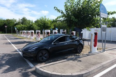 PALMANOVA, ITALY - Aug 17, 2021: Palmanova, Italy - August 17, 2021: A static shot of a solid black Tesla Model 3 long range awd charging at the new V3 Supercharger during summer. clipart