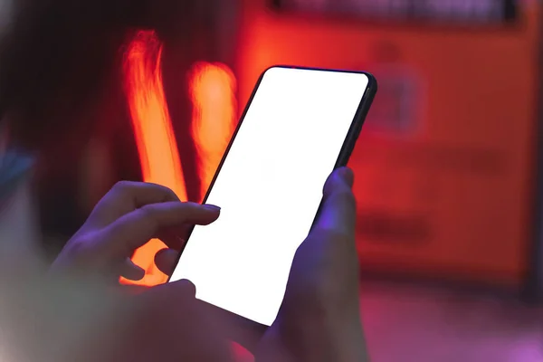 A selective focus of a person tapping on the screen of a mobile phone while standing at a street at night