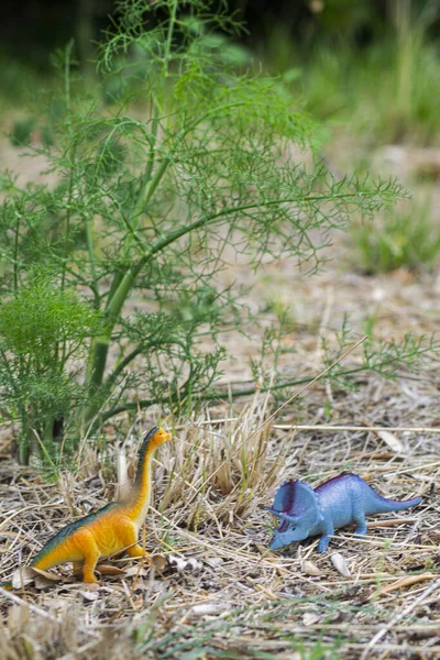 Pionowe Ujęcie Dwóch Kolorowych Małych Plastikowych Zabawek Dinozaurów Ziemi Zewnątrz — Zdjęcie stockowe