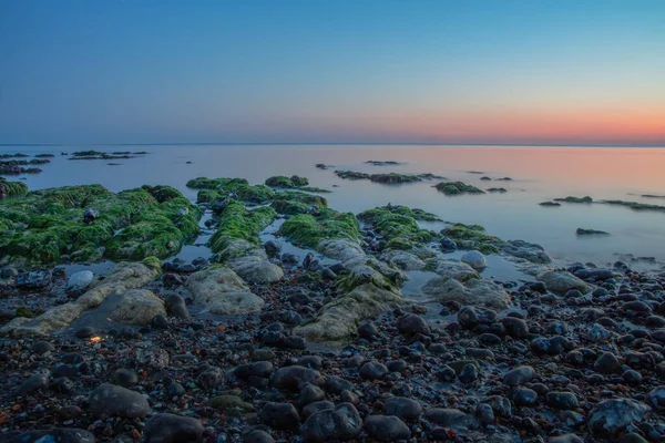 美丽的落日映照在平静的海洋上 岩石覆盖着苔藓 — 图库照片